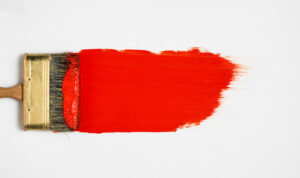 Brush with red paint lies on a white background, top view.
